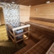 A bright sauna with wooden walls and benches, featuring a centrally placed stove protected by railings.